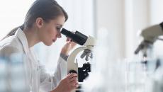 Healthcare worker looking through microscope in lab