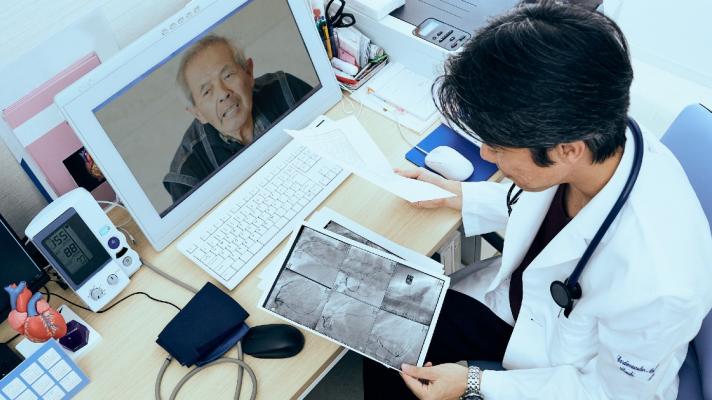 Person in lab attire looks at a scan image and talks to person via screen