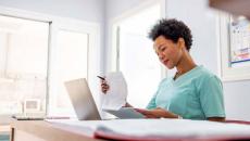 Healthcare worker looking at papers at a desk with a laptop