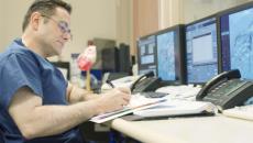 Healthcare worker taking notes in front of computer monitors