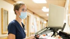 A nurse checking on a patient's file in a hallway laptop