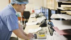 Surgeon in scrubs and cap leans before a computer