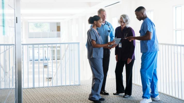 Nurses huddled together look at electronic health records on a tablet.