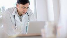 A doctor looking over a patient's medical record on a laptop