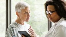 A senior patient consulting with a doctor who is holding a digital tablet