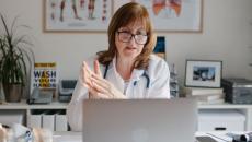 A doctor using a laptop is in an online video consultation with a patient